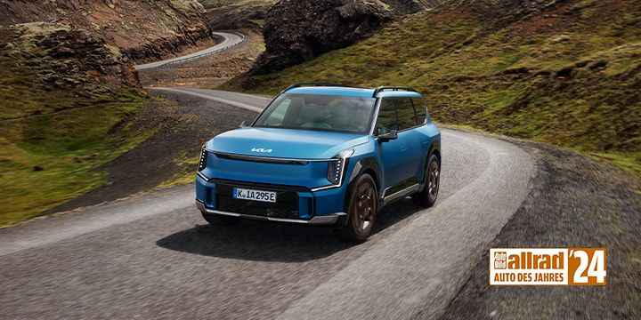 Kia EV9, Goldenes Lenkrad, Frau steht vor EV9